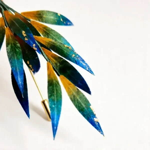 Detail view of handcrafted gradient silk leaf brooch Close-up of blue green silk leaf brooch with gold accents
